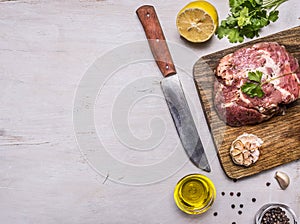 Raw pork steak with spices, garlic and herbs, lemon and butter knife for meat, border, place for text on wooden rustic background