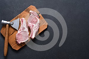 Raw pork steaks on a board with an ax on a dark background. View from above. Fresh meat. Ribs