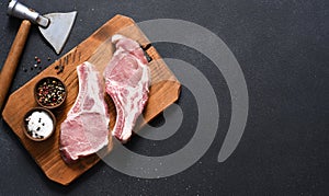 Raw pork steaks on a board with an ax on a dark background. View from above. Fresh meat. Ribs