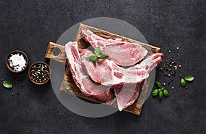 Raw pork steaks on a board with spices and basil on a dark background. Top view. Fresh meat. Ribs