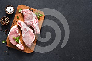 Raw pork steaks on a board with spices and basil on a dark background. Top view. Fresh meat. Ribs