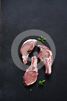 Raw pork steaks on a board with spices and basil on a dark background. Top view. Fresh meat. Ribs