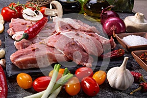 Raw pork steaks, fresh vegetables, spices close-up on a textured background