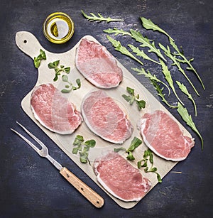 Raw pork steaks for grilling, with herbs, butter and meat fork, on a cutting board wooden rustic background top view close up