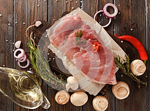 Raw pork tenderloin with mushrooms, chili pepper, onion, olive oil, rosemary, salt on a dark wooden background