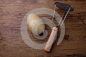 A raw potatoe on a wood table with a tool for crushing