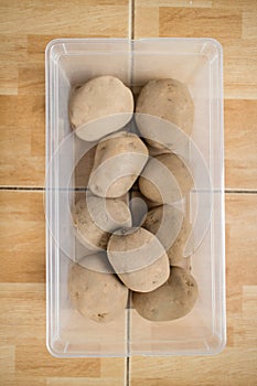 Raw potatoes in a plastic container on floor