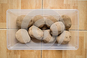 Raw potatoes in a plastic container on floor