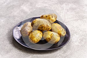 Raw potatoes on plate on concrete background