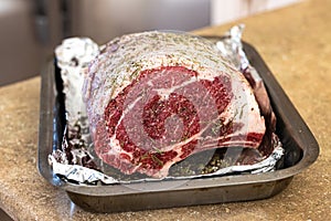 Raw prime rib roast seasoned and sitting on an aluminum foil lined pan ready for the oven for a holiday Christmas dinner