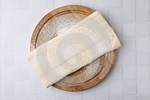 Raw puff pastry dough on white tiled table, top view