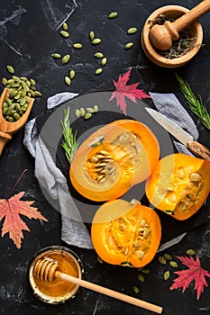 Raw pumpkin with herbs, seeds and honey on a black stone background. Autumn food background. Thanksgiving and halloween holiday