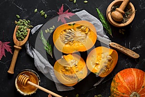 Raw pumpkin with herbs, seeds and honey on a black stone background. Autumn food background. Thanksgiving and halloween holiday