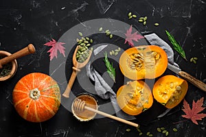 Raw pumpkin with herbs, seeds and honey on a black stone background. Autumn food background. Thanksgiving and halloween holiday