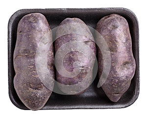 Raw purple potatoes on black plastic food tray isolated on white background. Top view