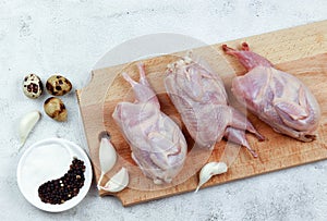 Raw quails on a wooden cutting board on a light gray background