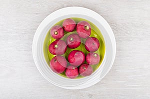 Raw radishes in green glass plate on wooden table