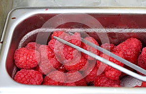 Raw raspberries in a bin with tongs