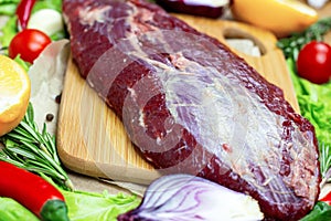 Raw red beef meat with green rosemary and fresh vegetables on light wooden cutting board background.