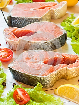 Raw red fish steak with lemon and spices and fresh vegetables on light background