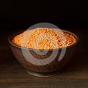Raw red lentils in clay bowl on vintage wooden background.