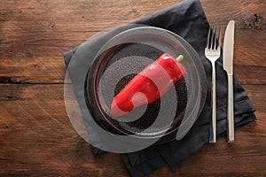 Raw red pointed sweet pepper on a dark plate, cutlery and napkin on a rustic wooden background, healthy eating concept or