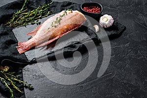 Raw red sea bass on a stone Board with thyme. Black background. Top view. Space for text