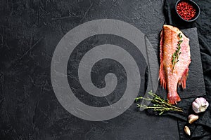 Raw red sea bass on a stone Board with thyme. Black background. Top view. Space for text