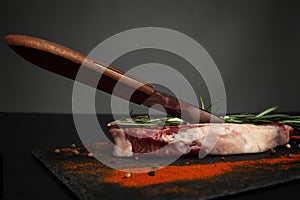 Raw ribeye steak with seasonings and a knife. A piece of marbled beef with rosemary and a mixture of peppercorns. Side view,