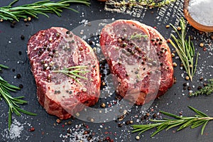 Raw Ribeye steaks with salt and herbs on grey board. Top view
