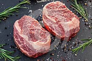 Raw Ribeye steaks with salt and herbs on grey board. Top view