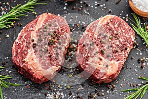 Raw Ribeye steaks with salt and herbs on grey board. Top view