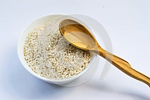 Raw rice in white plate and wooden spoon