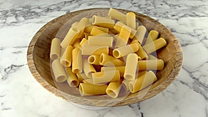 raw rigatoni pasta falling in to wooden plate. slow motion
