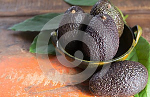 Raw ripe dark green avocados with leaves on wooden background