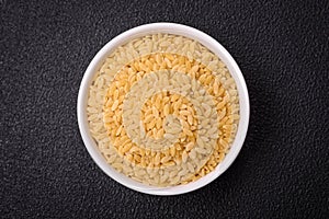 Raw risoni pasta made from durum wheat on a dark concrete background