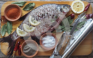 Raw river bream fish, prepared for baking in the oven with lemon slices and seasoning on a wooden board