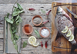 Raw river bream fish, prepared for baking in the oven with lemon slices and seasoning on a wooden board. Top view