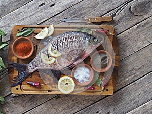 Raw river bream fish, prepared for baking in the oven with lemon slices and seasoning on a wooden board. Top view,place for text