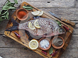 Raw river bream fish, prepared for baking in the oven with lemon slices and seasoning on a wooden board. Top view,place for text