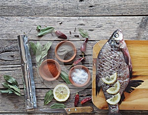 Raw river bream fish, prepared for baking in the oven with lemon slices and seasoning on a wooden board. Top view,place for text