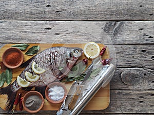 Raw river bream fish, prepared for baking in the oven with lemon slices and seasoning on a wooden board.Top view, place for text