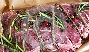 Raw roast beef with herbs tied with a rope with cooking ingredients, on perchment background, top view