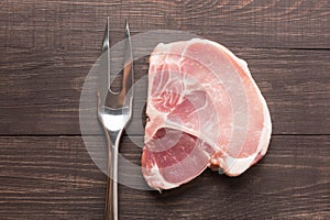 Raw roast meat and meat fork on wooden background