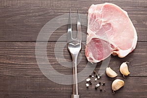 Raw roast meat and meat fork on wooden background