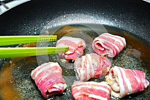 Raw rolls with bacon are fried in a pan. Cooking junk and fatty foods
