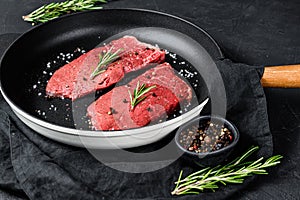 Raw rump steak in a frying pan. Beef meat. Black background. Top view