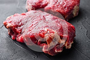 Raw rump steaks over black textured  background, side view selective focus