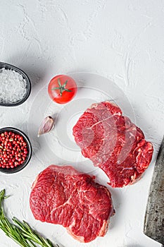 Raw rumpsteak, farm beef meat with seasonings, rosemary, garlic and butcher cleaver. White textured background. Top view vertical