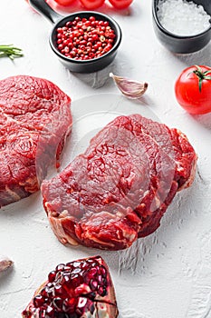 Raw rumpsteak, farm beef meat with seasonings, rosemary, garlic, garnet. White textured background. Side view